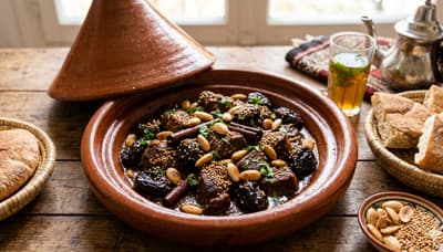 Moroccan meat and prune tagine presented in a traditional clay pot, garnished with almonds and sesame seeds