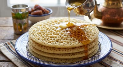 Stack of baghrir pancakes with holes, drizzled with honey