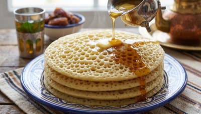 Stack of baghrir pancakes with holes, drizzled with honey